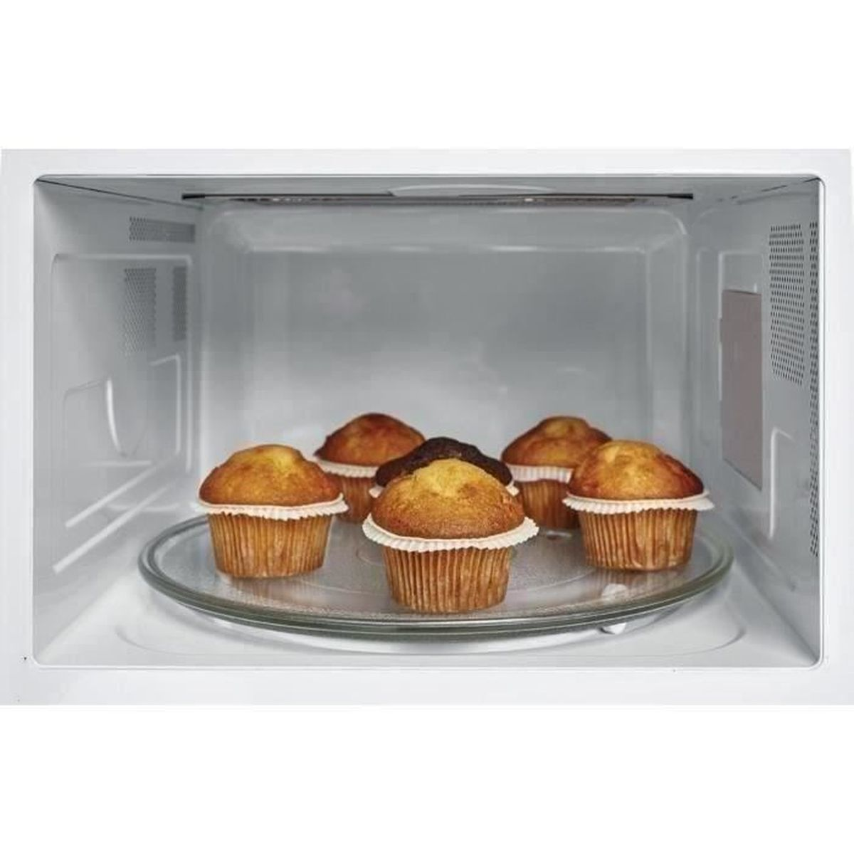 Cinque muffin su un piatto di vetro dentro un forno a microonde, pronti per essere riscaldati.