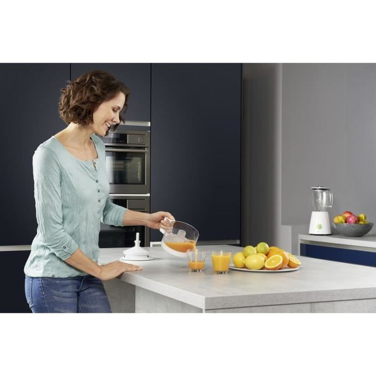 Donna versa succo in bicchieri in una cucina moderna. Arance e limoni su un piatto.