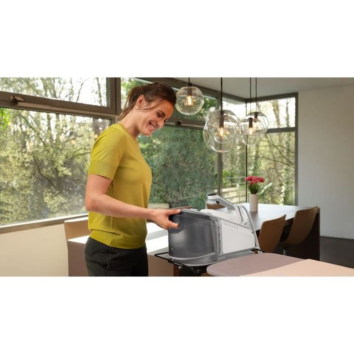 Een vrouw in een groen shirt bereidt het strijkijzer voor, in een kamer met lampen.