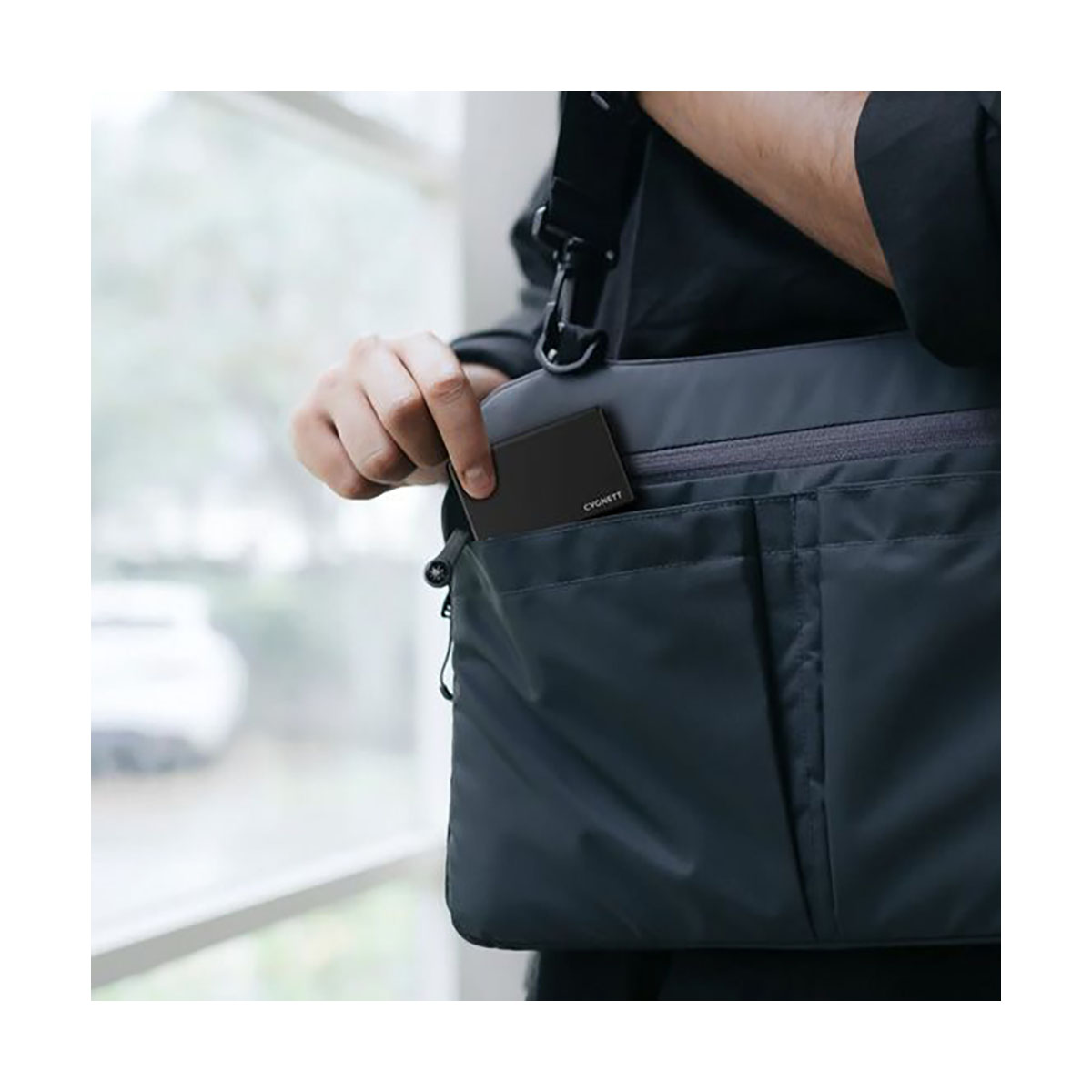 Die Hand einer Person nimmt ein schwarzes Objekt aus einer grauen Tasche. Weißer Hintergrund.