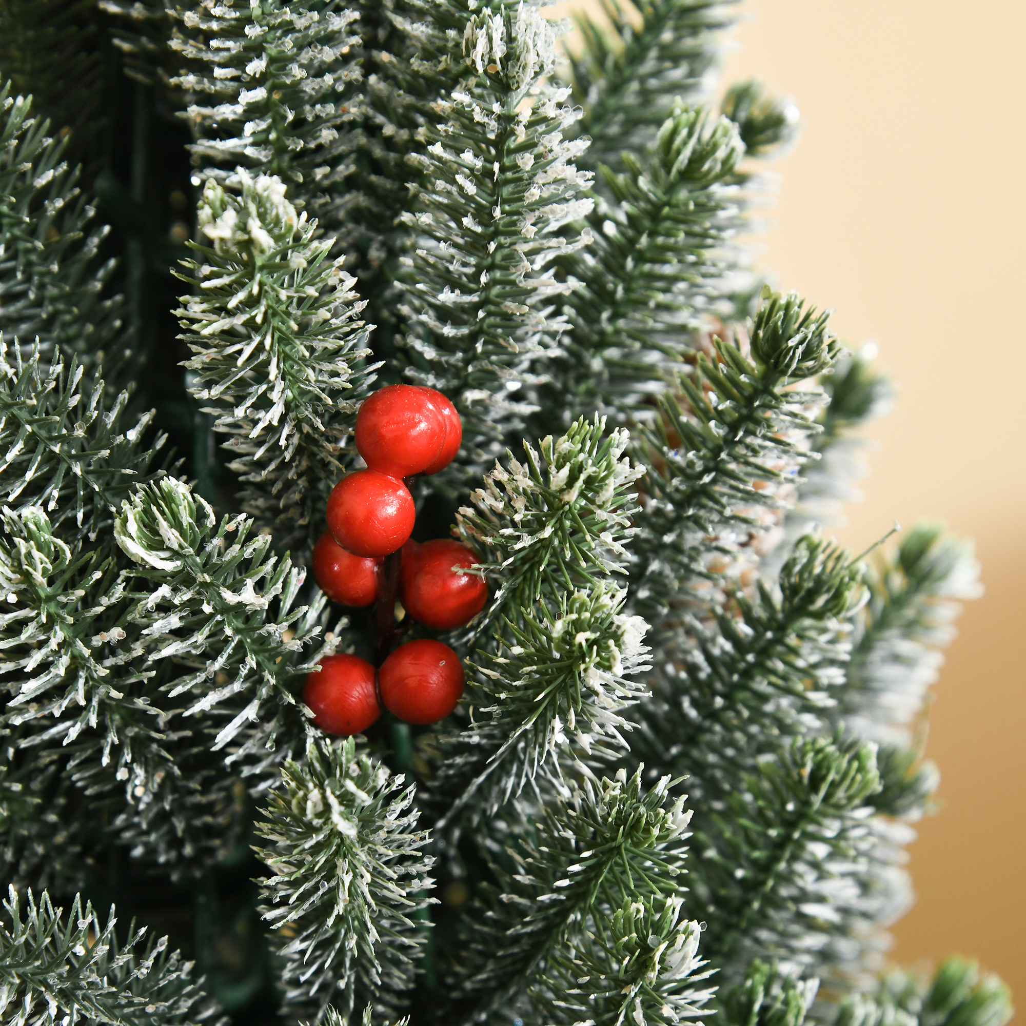 Nahaufnahme von künstlichen Weihnachtsbaumzweigen mit roten Beeren und Schnee. Die Zweige sind grün und weiß.