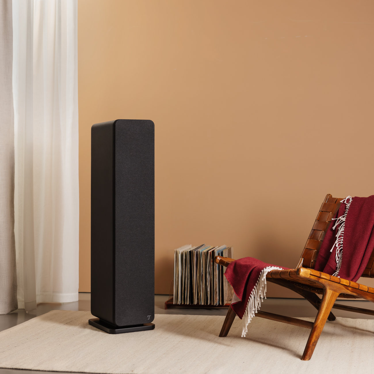 Ein schwarzer Lautsprecher mit einer roten Decke auf einem Holzstuhl und einer Vinyl-Schallplattensammlung.