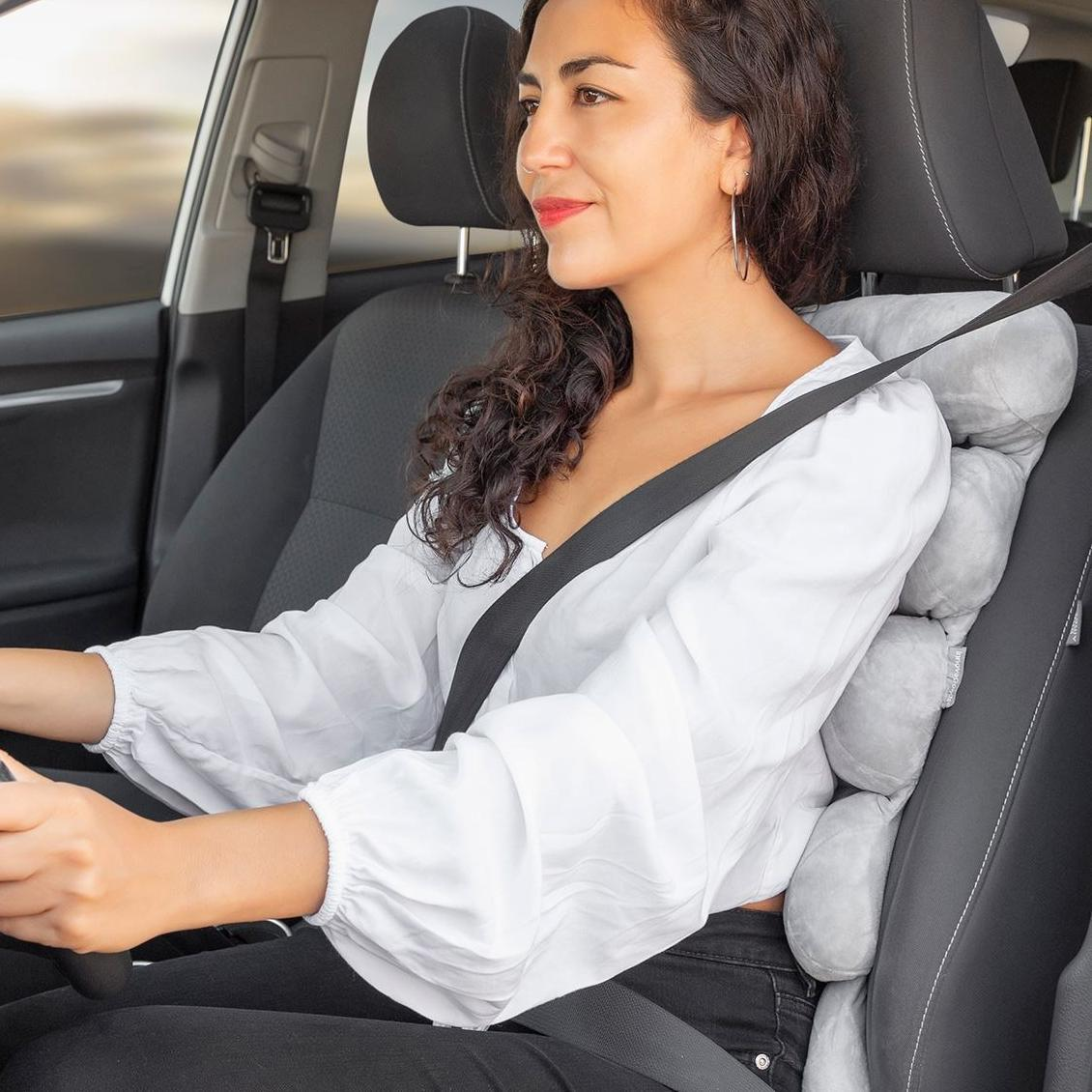 Frau fährt Auto, trägt Sicherheitsgurt, mit Rückenstützkissen auf dem Sitz.