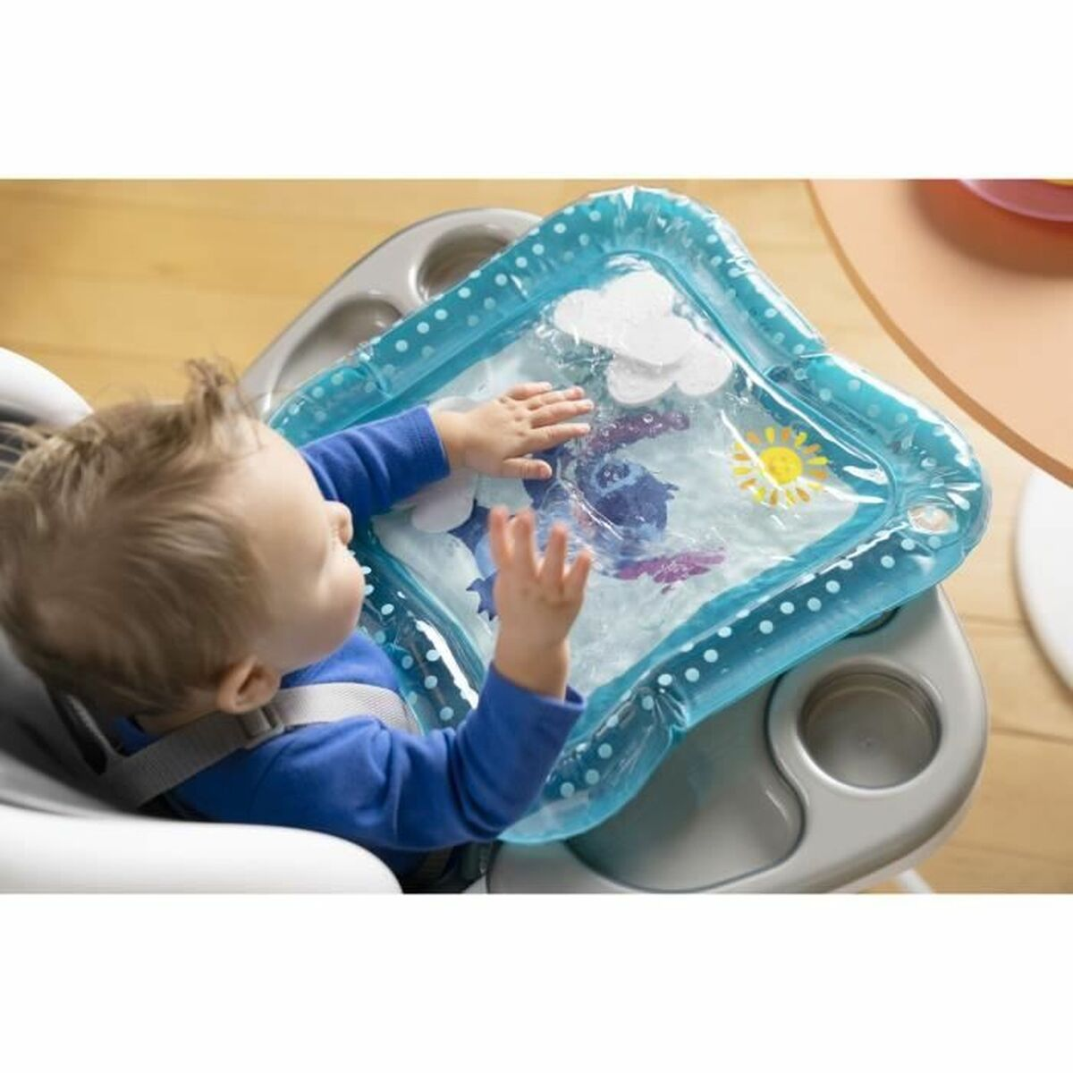Ein Baby sitzt in einem Hochstuhl und spielt mit einer Wassermatte mit Meerestieren und einer Sonne darauf.