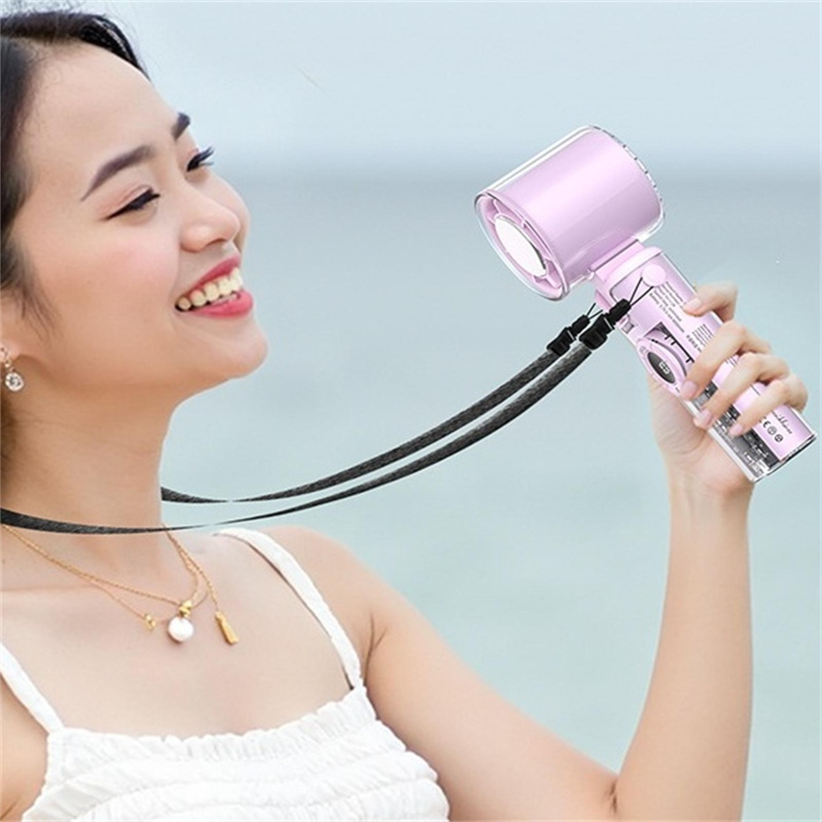 Frau lächelt, während sie einen rosa Handventilator mit schwarzem Riemen hält. Der Hintergrund ist das Meer.