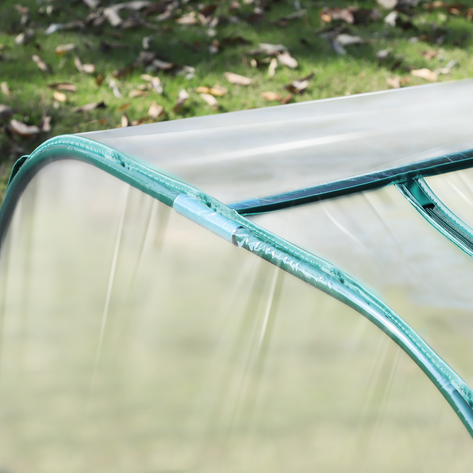 Una vista de cerca de un pequeño invernadero con una cubierta de plástico transparente y un marco verde. El fondo está borroso.