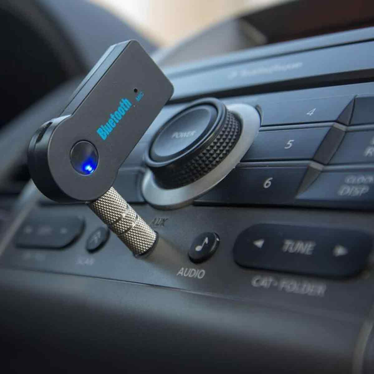Ein schwarzer Bluetooth-Empfänger, der in ein Autoradio-System eingesteckt ist, mit Knöpfen und einem Drehregler auf dem Armaturenbrett.