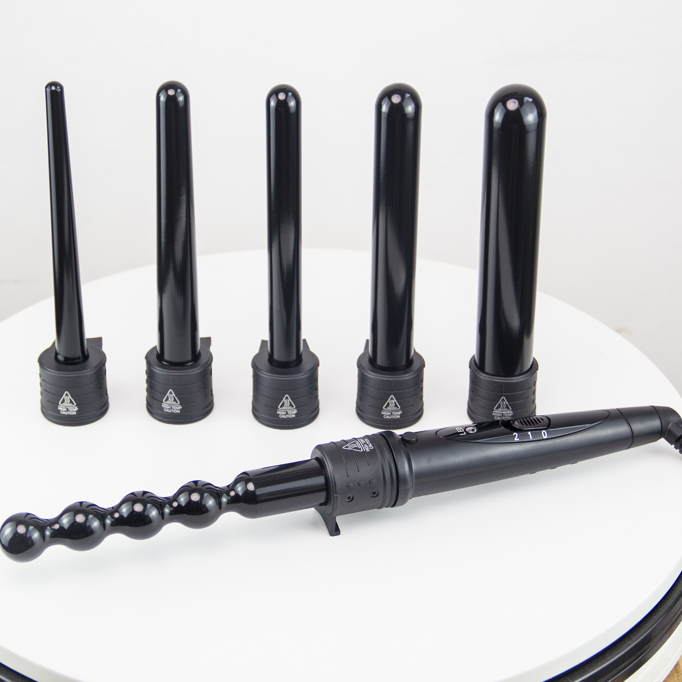 Sechs schwarze Lockenstäbe in verschiedenen Größen und ein Lockenstab auf einer weißen Oberfläche.