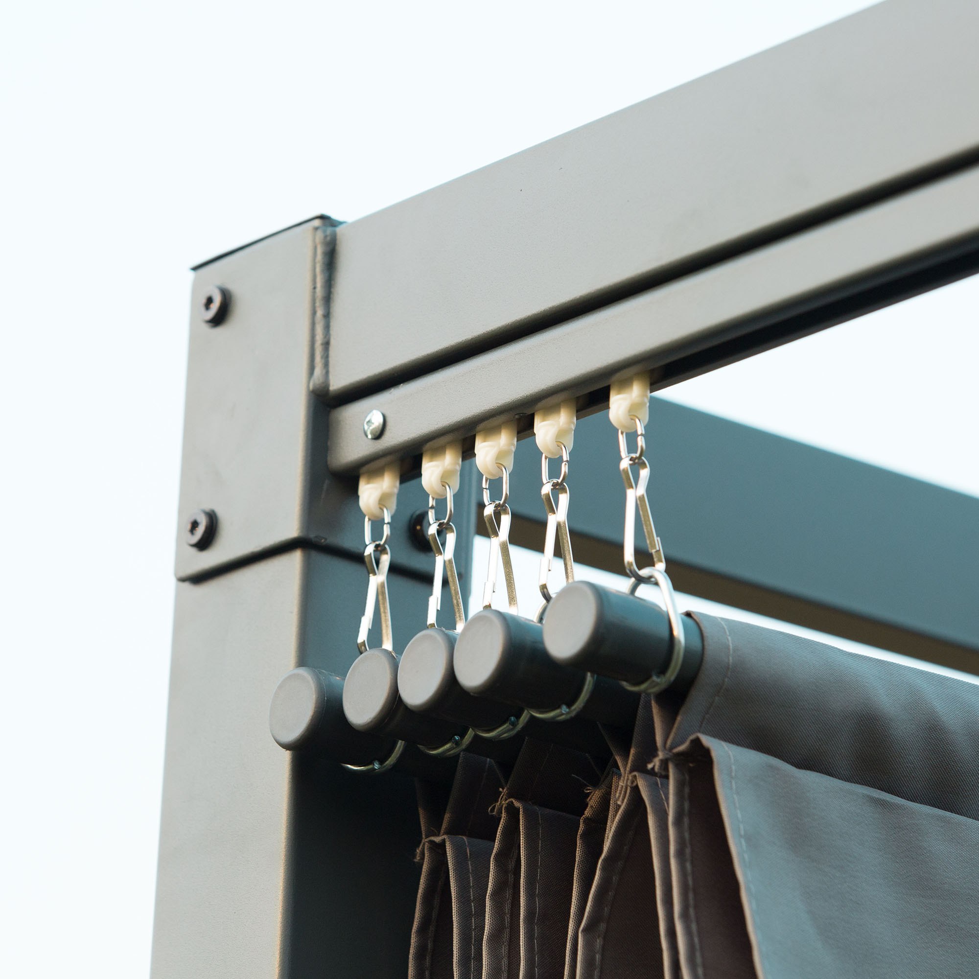 Nahaufnahme der hängenden Schatten der Pergola. Graue Stoffschatten hängen an einem grauen Metallrahmen mit Haken.