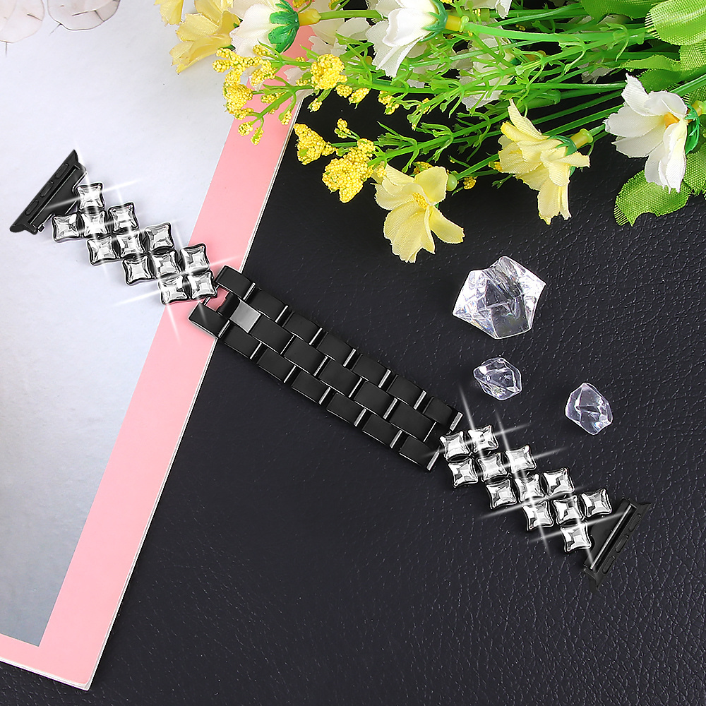 Schwarzes und silbernes Uhrenarmband mit Diamanten. Das Band liegt auf schwarzem Untergrund mit anderen Dekorationen. Blumen im Hintergrund.
