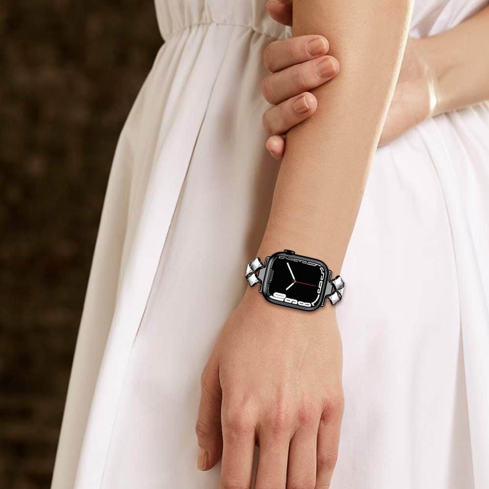 Handgelenk einer Frau mit einer Apple Watch. Die Uhr hat einen schwarzen Bildschirm und ein diamantbesetztes Armband. Die Frau trägt ein weißes Kleid.