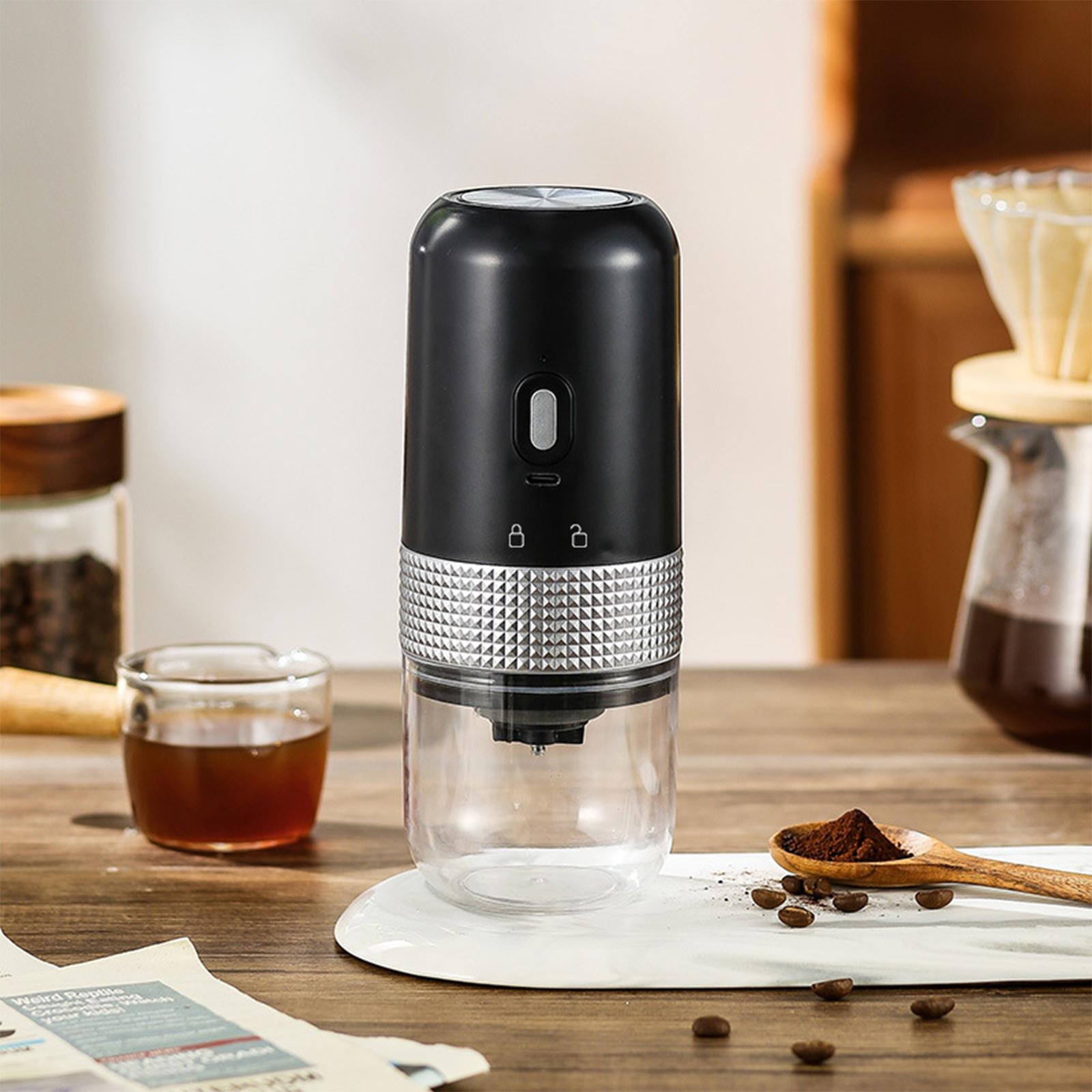 Ein schwarzer und silberner tragbarer Kaffeemühle mit Kaffeesatz im Glasbehälter und einem Holzlöffel.
