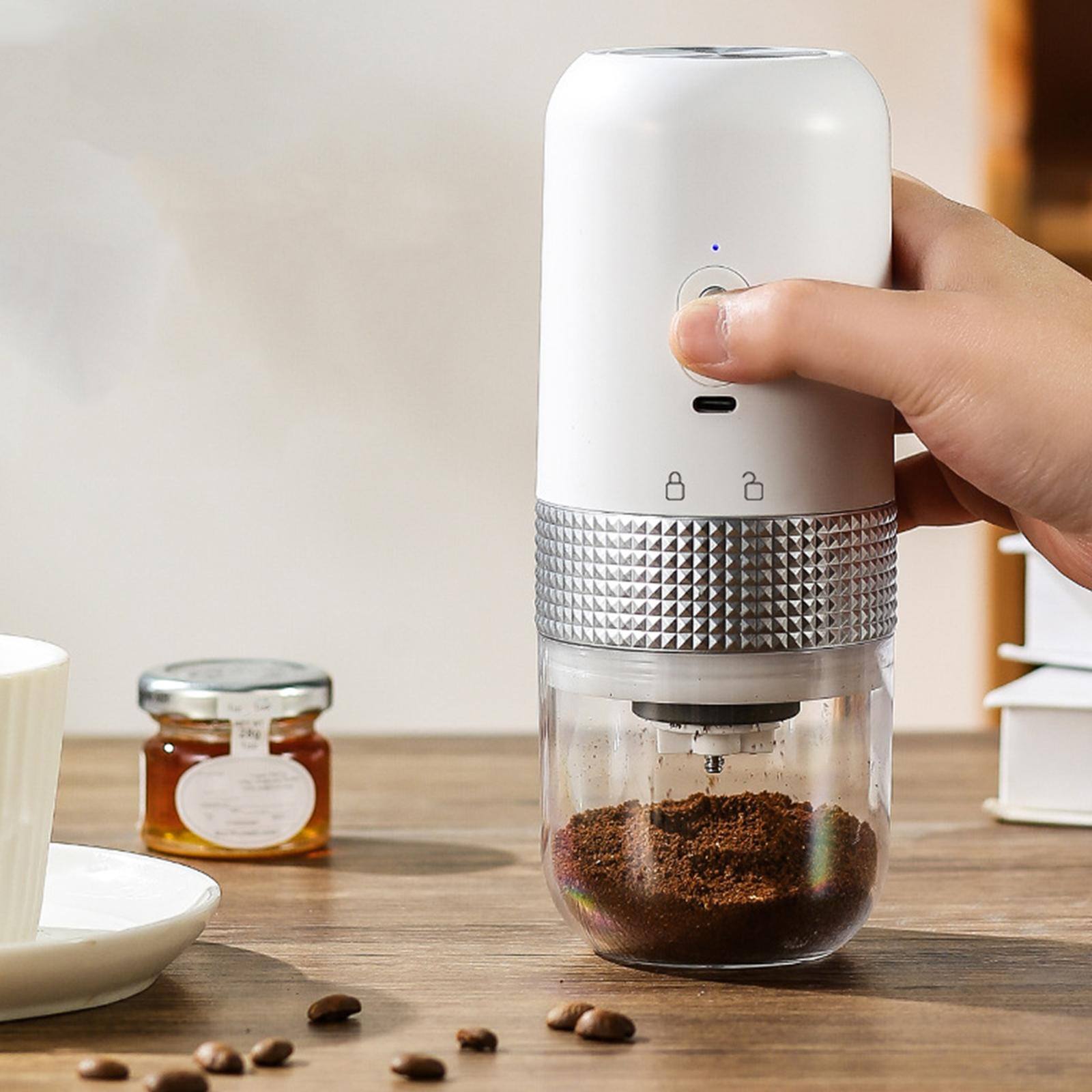 Eine Hand bedient einen weißen, tragbaren Kaffeemühle mit Kaffeesatz im durchsichtigen Behälter.