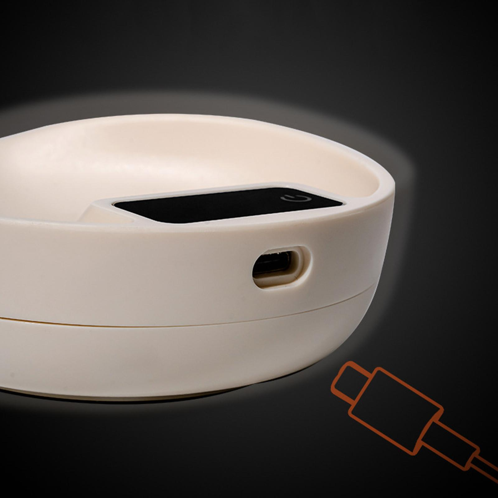 Cremefarbene schalenförmige Vorrichtung mit kleinem Bildschirm und USB-Anschluss, vor dunklem Hintergrund.