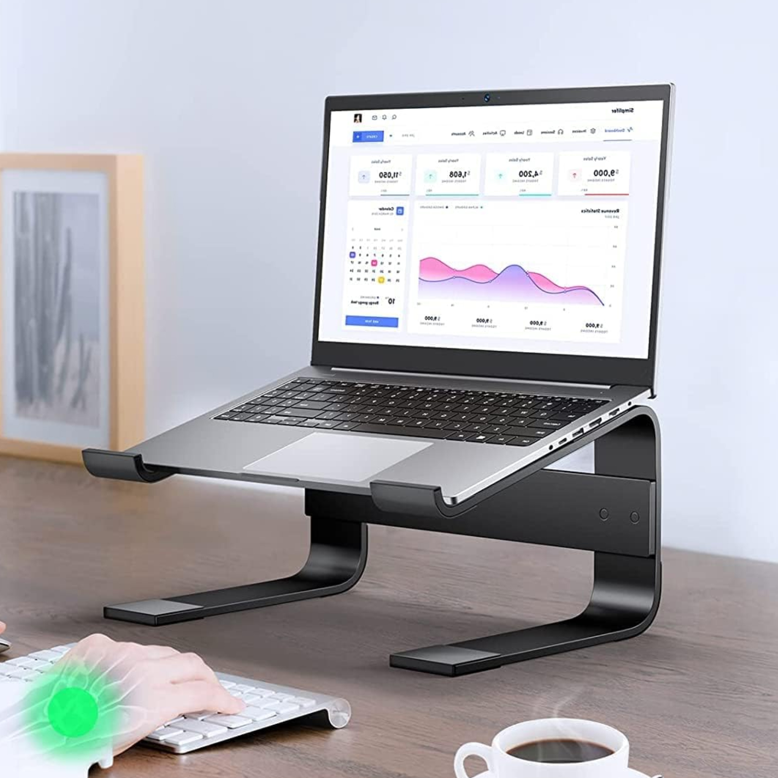 Ein Laptop steht auf einem schwarzen Ständer auf einem Holztisch. Eine Hand ist in der Nähe einer Tastatur.