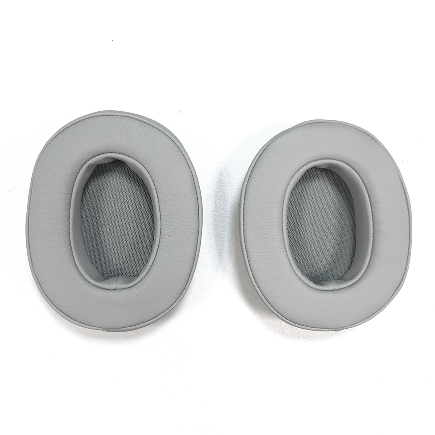 Dwie szare nausznice do słuchawek, owalne z siateczkowym środkiem, na białym tle.