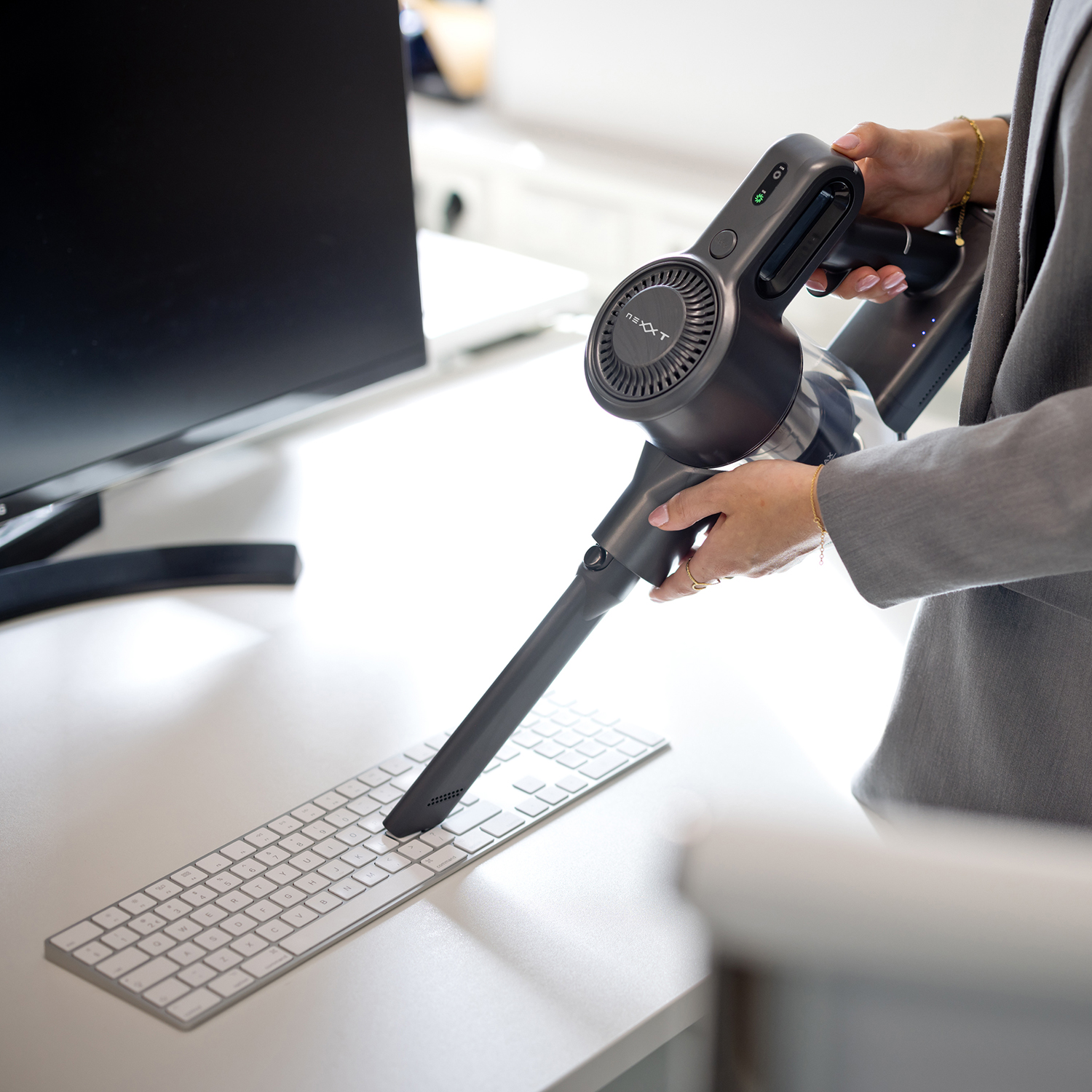 A person using a black and gray vacuum cleaner to clean a white keyboard.