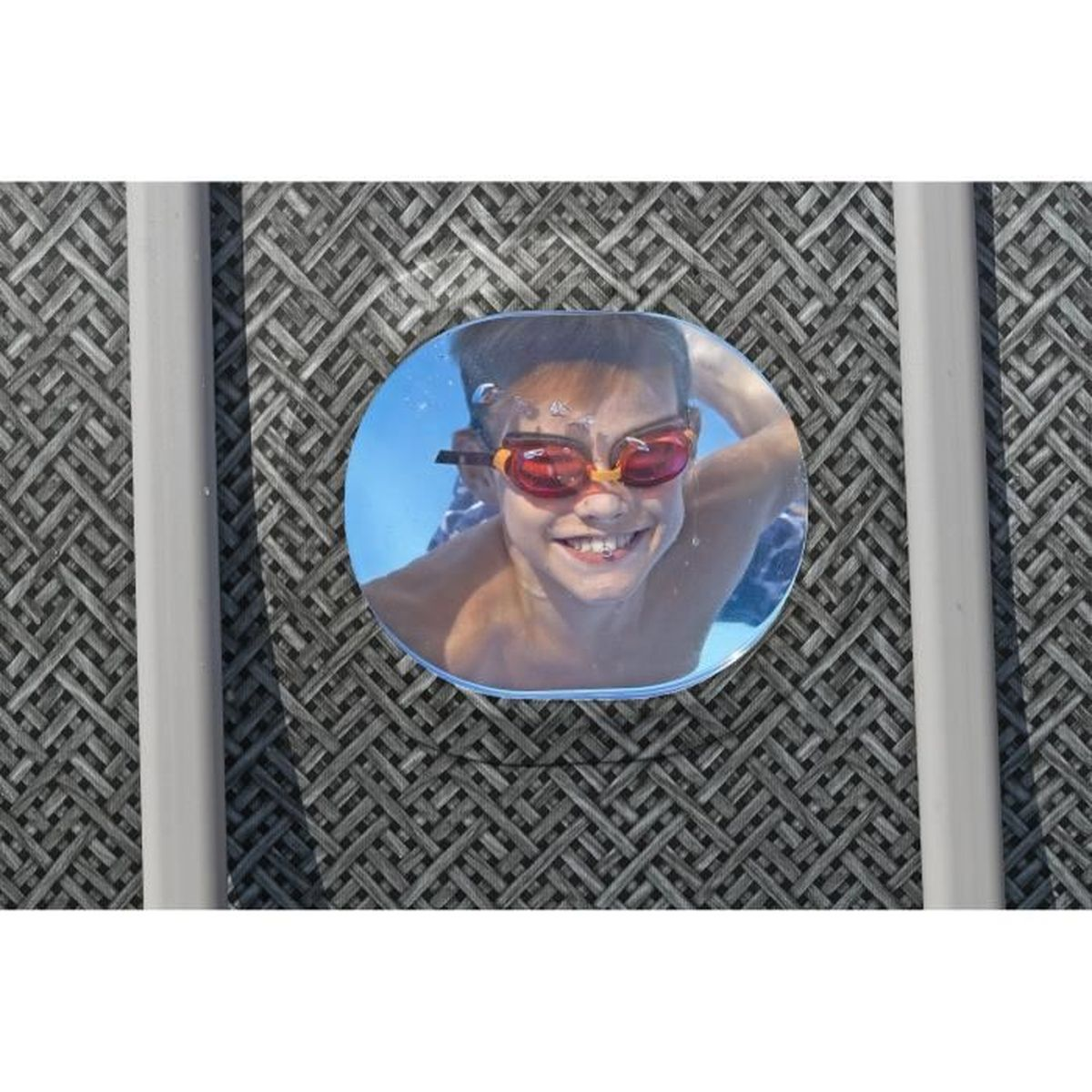 Chłopiec w okularach pod wodą, uśmiechający się przez bulaj, osadzony w szarej powierzchni.