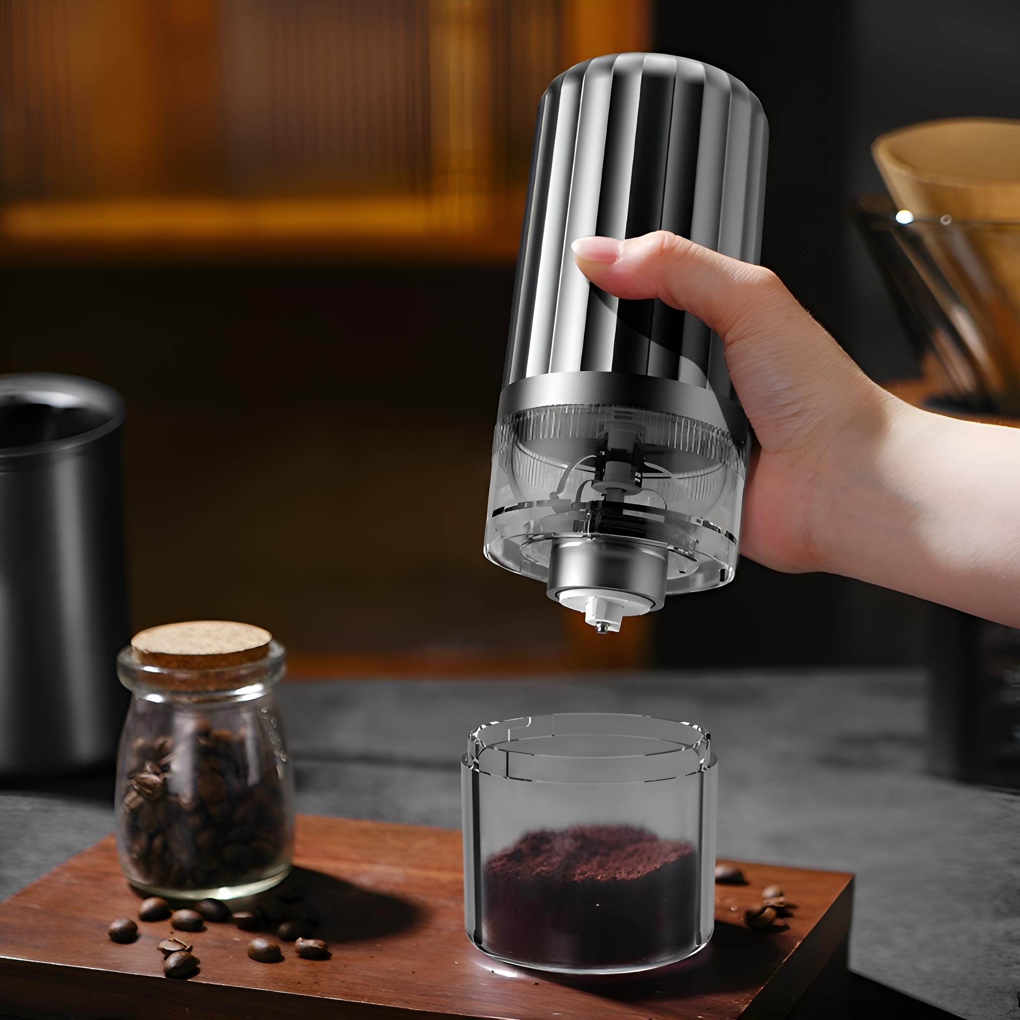 Eine Hand hält eine Kaffeemühle und gießt gemahlenen Kaffee in einen Glasbehälter. Bohnen und Glas im Hintergrund.