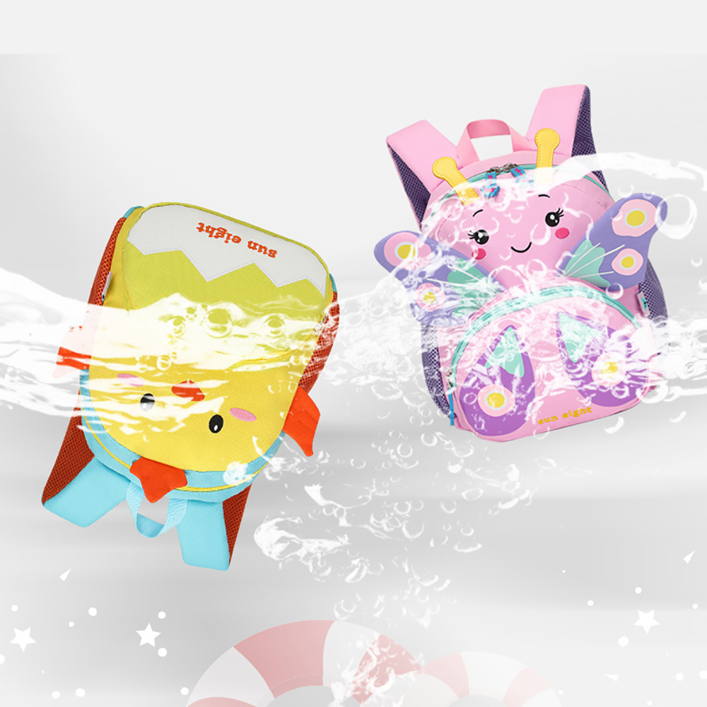 Zwei Kinderrucksäcke, ein gelbes Küken und ein rosa Schmetterling, werden vor einem weißen Hintergrund mit Wasser bespritzt.