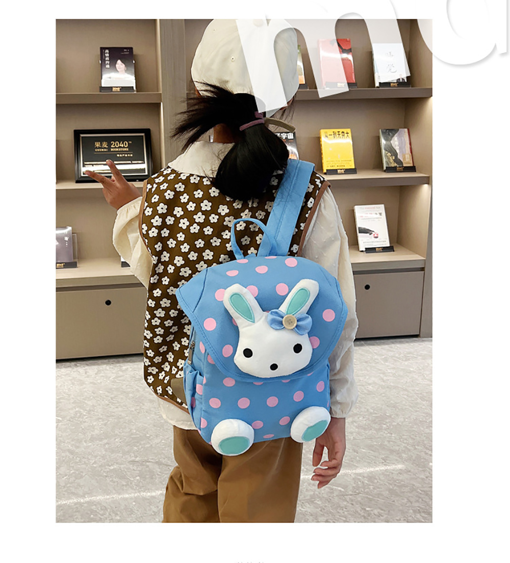 Ein Kind trägt einen hellblauen Rucksack mit Tupfen, einem weißen Hasengesicht und Schleifendetail.