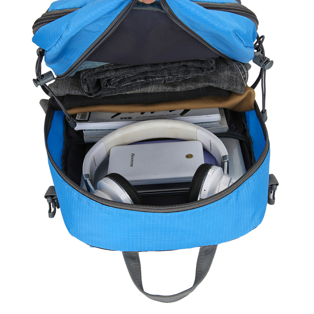 Ein offener blauer Rucksack, gefüllt mit Gegenständen wie Kleidung, Büchern, Kopfhörern und einem Tablet.