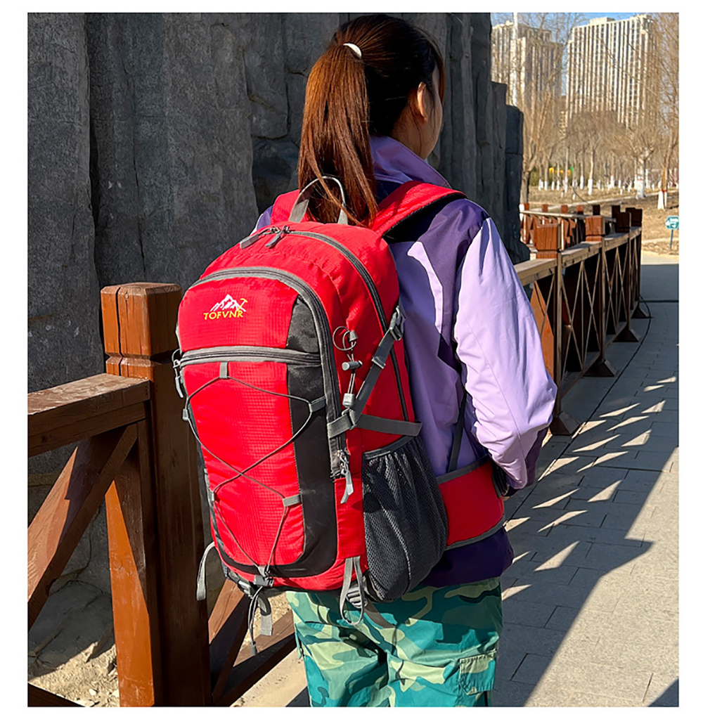 Eine Frau mit Pferdeschwanz trägt eine lila Jacke und einen roten Rucksack und steht nach links gerichtet.