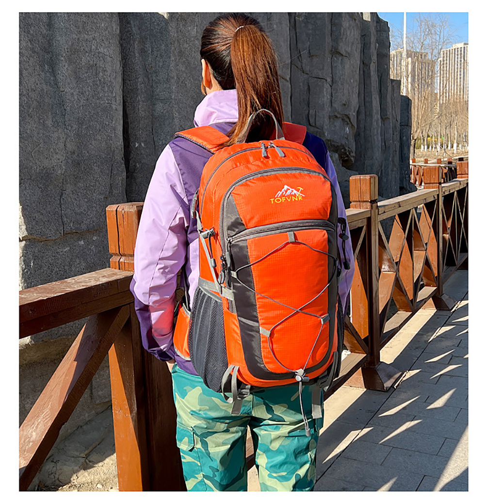 Eine Frau mit Pferdeschwanz, lila Jacke und orangefarbenem Rucksack steht an einem Holzzaun.