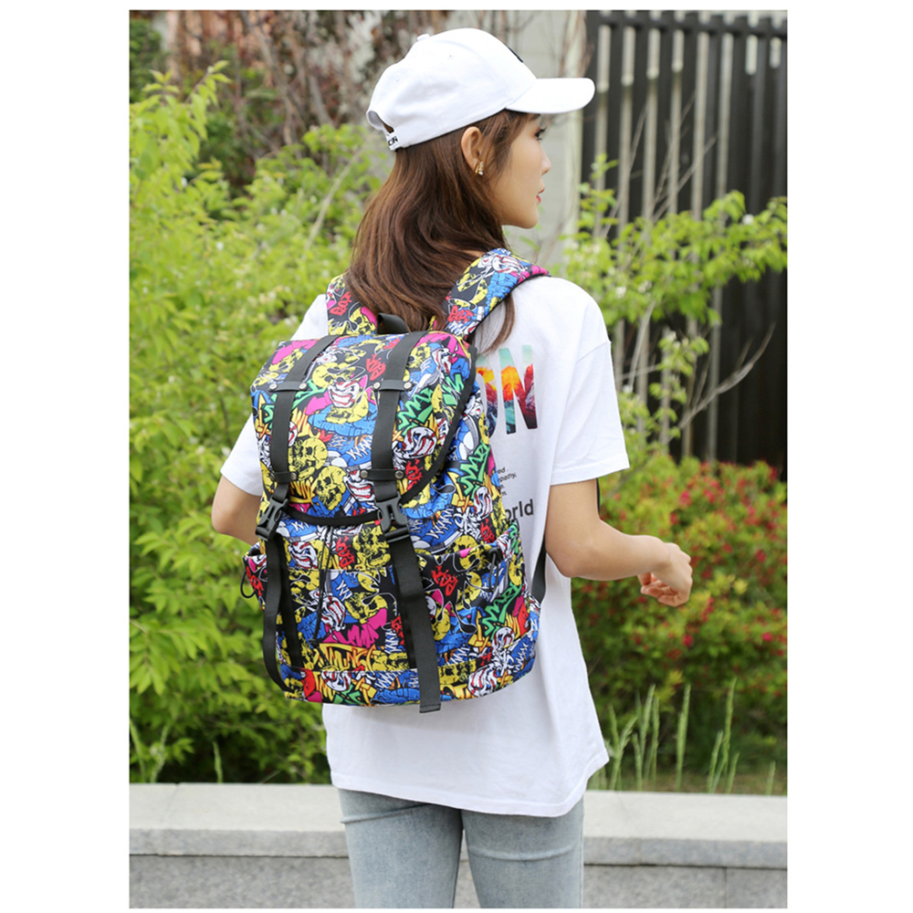 Eine Frau mit einem Rucksack im Graffiti-Design. Sie trägt ein weißes Hemd und eine weiße Kappe. Grüne Büsche im Hintergrund.