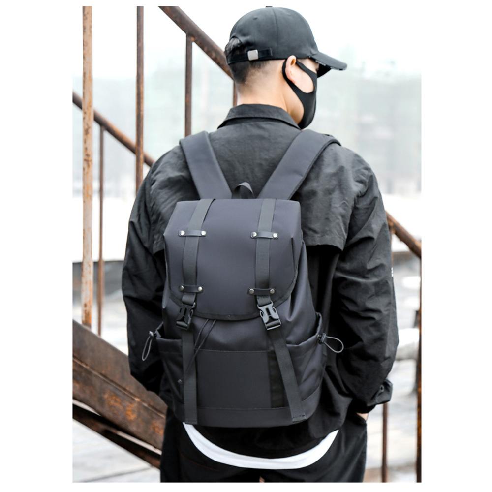 Ein Mann in Schwarz, der einen schwarzen Rucksack, eine Kappe und eine Maske trägt, steht vor Metallstäben.