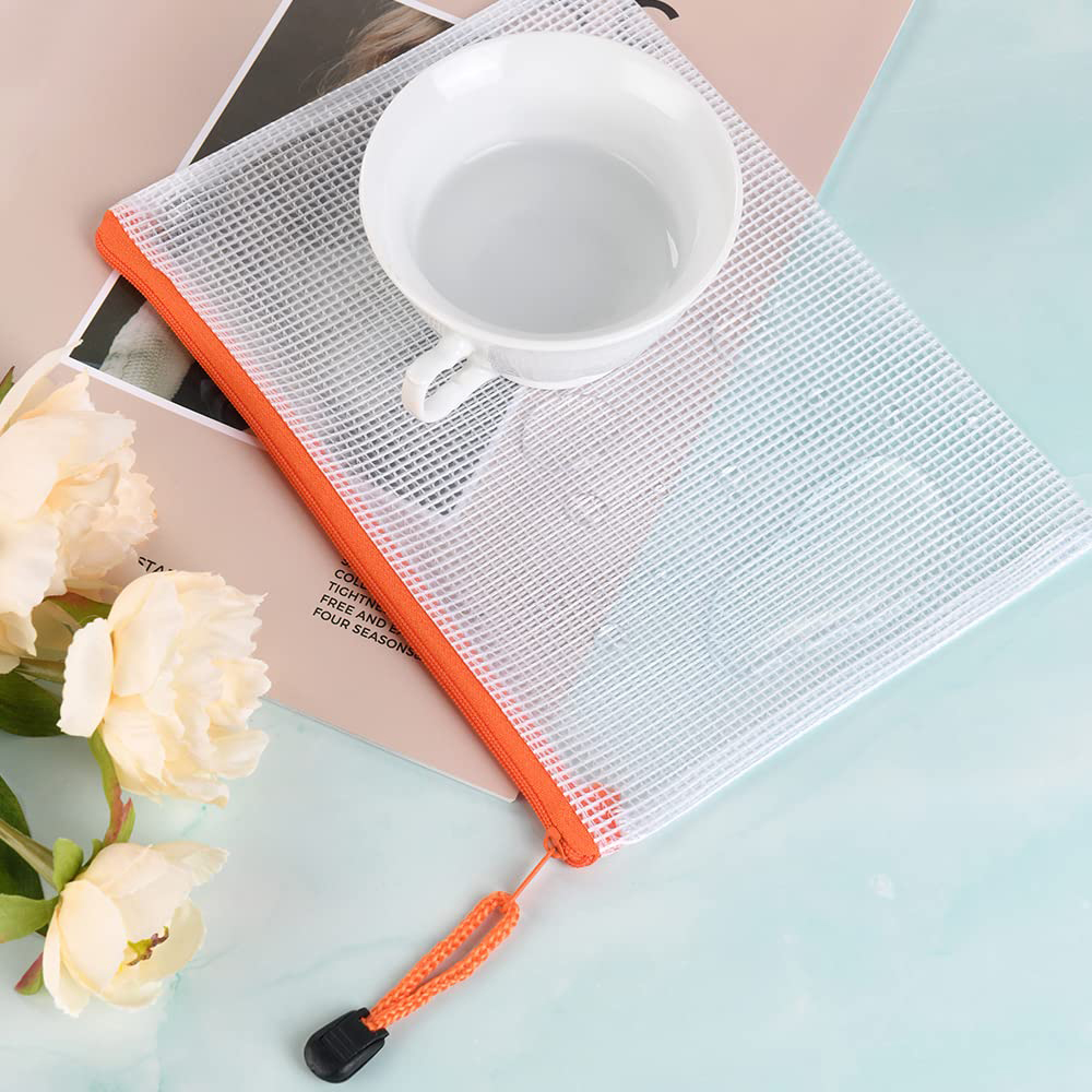 Eine weiße Tasse auf einem Mesh-Beutel mit orangefarbenem Reißverschluss. Blumen sind im Vordergrund.