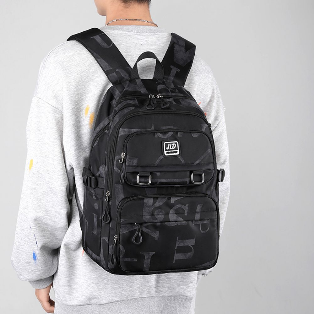 Ein Mann trägt einen grauen Pullover und einen schwarzen Rucksack mit Buchstaben bedruckt.
