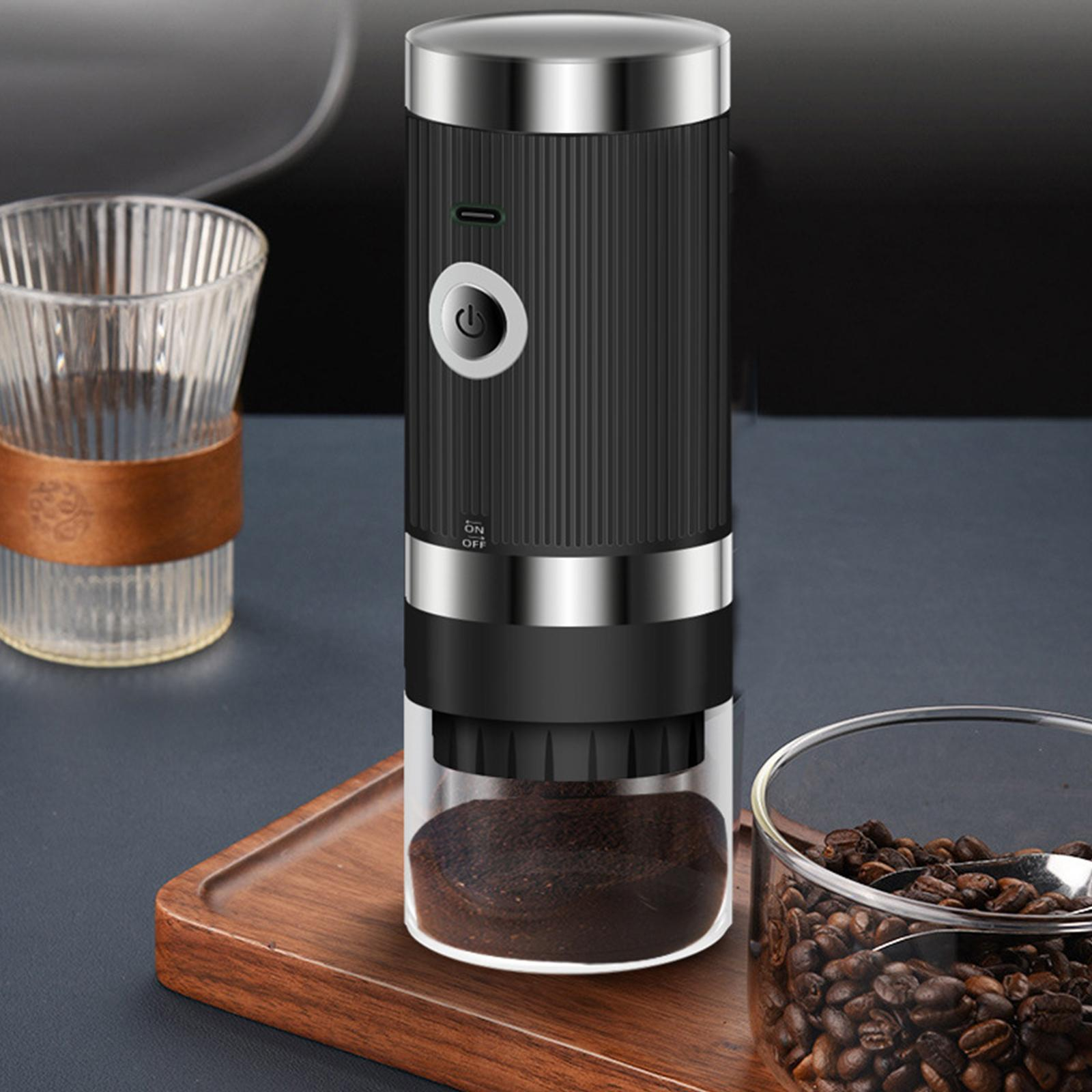 Eine Kaffeemühle steht auf einem Tisch mit Kaffeebohnen und einem Glas. Die Mühle ist schwarz-silberfarben mit Kaffeesatz.