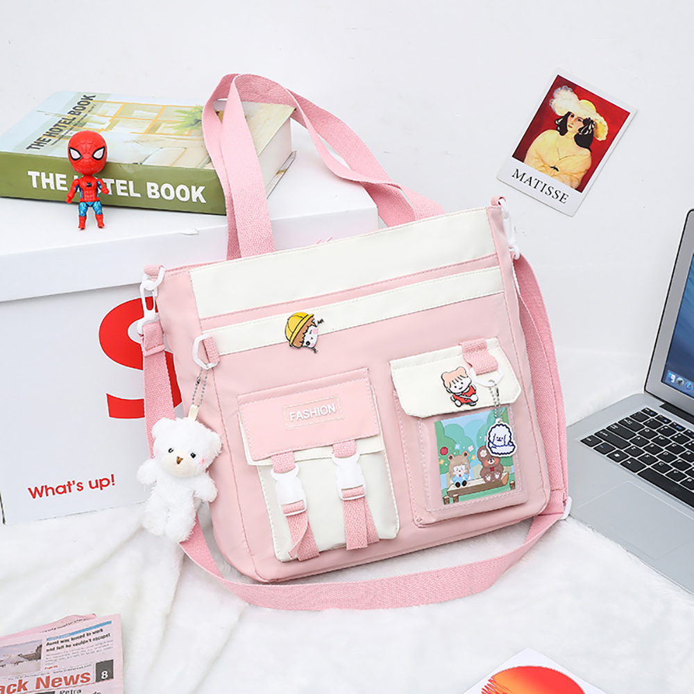 Rosa-weiße Tragetasche mit mehreren Taschen. Sie hat Verzierungen und einen Gurt. Im Hintergrund ist ein Laptop.