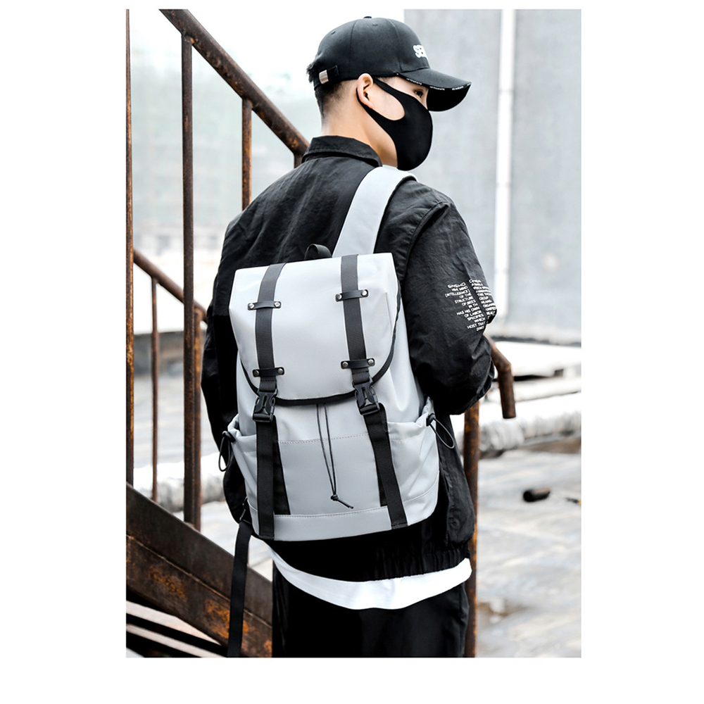 Mann mit schwarzer Maske, Mütze und Jacke, mit grauem Rucksack. Draußen, in der Nähe von Metallstruktur.