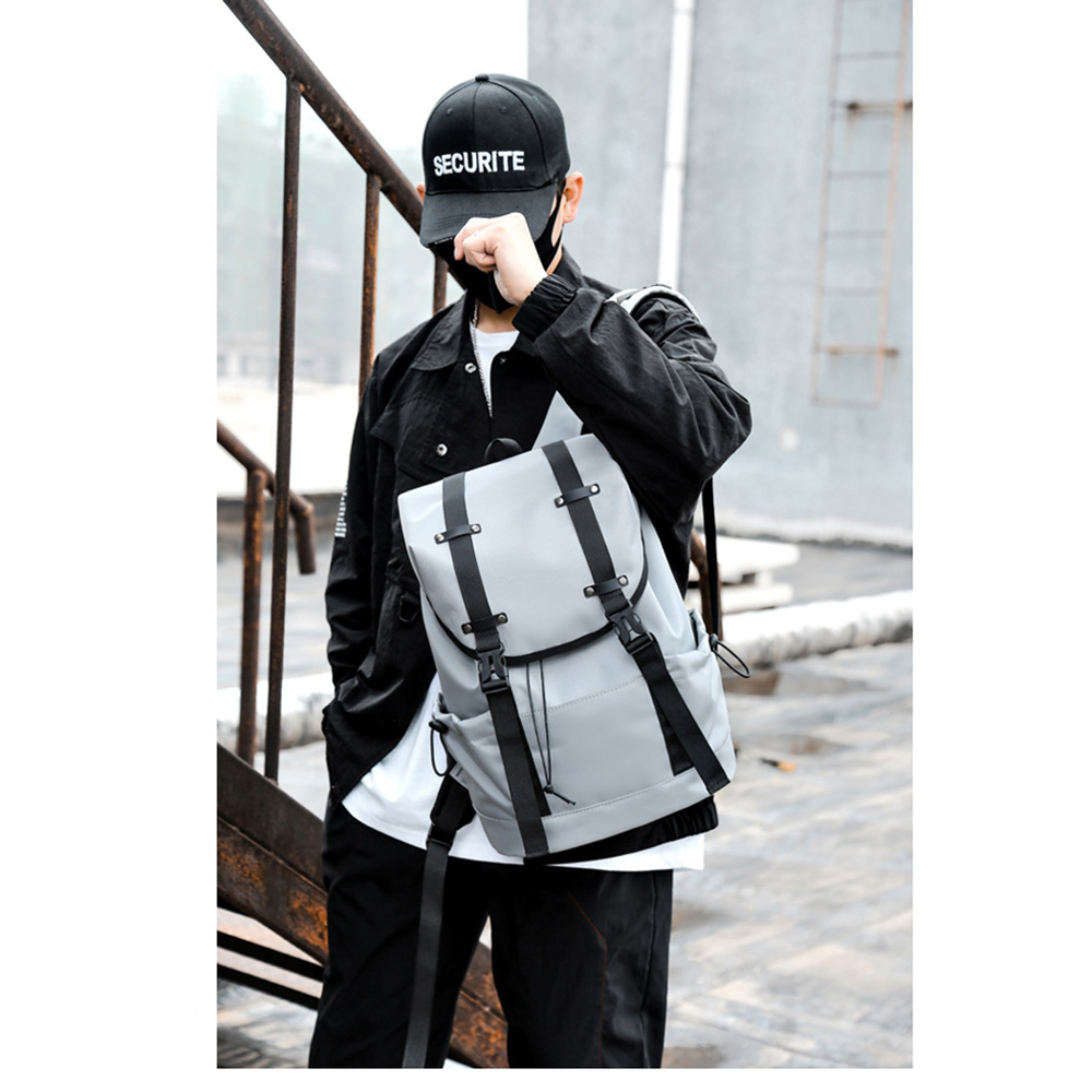 Mann in schwarzer Kappe und Jacke mit grauem Rucksack, in der Nähe einer Metallstruktur. Maskiert.