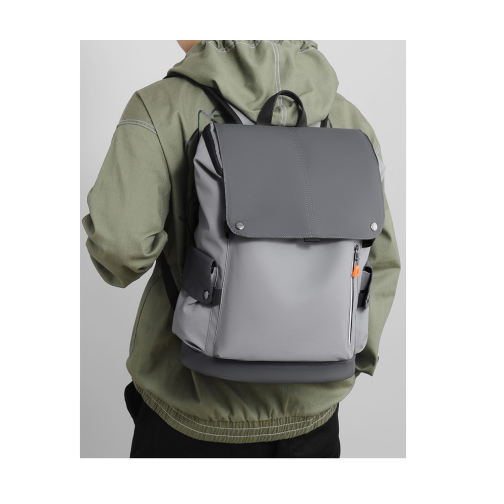 Eine Person trägt einen grauen Rucksack mit Klappe und Taschen vor einem weißen Hintergrund.