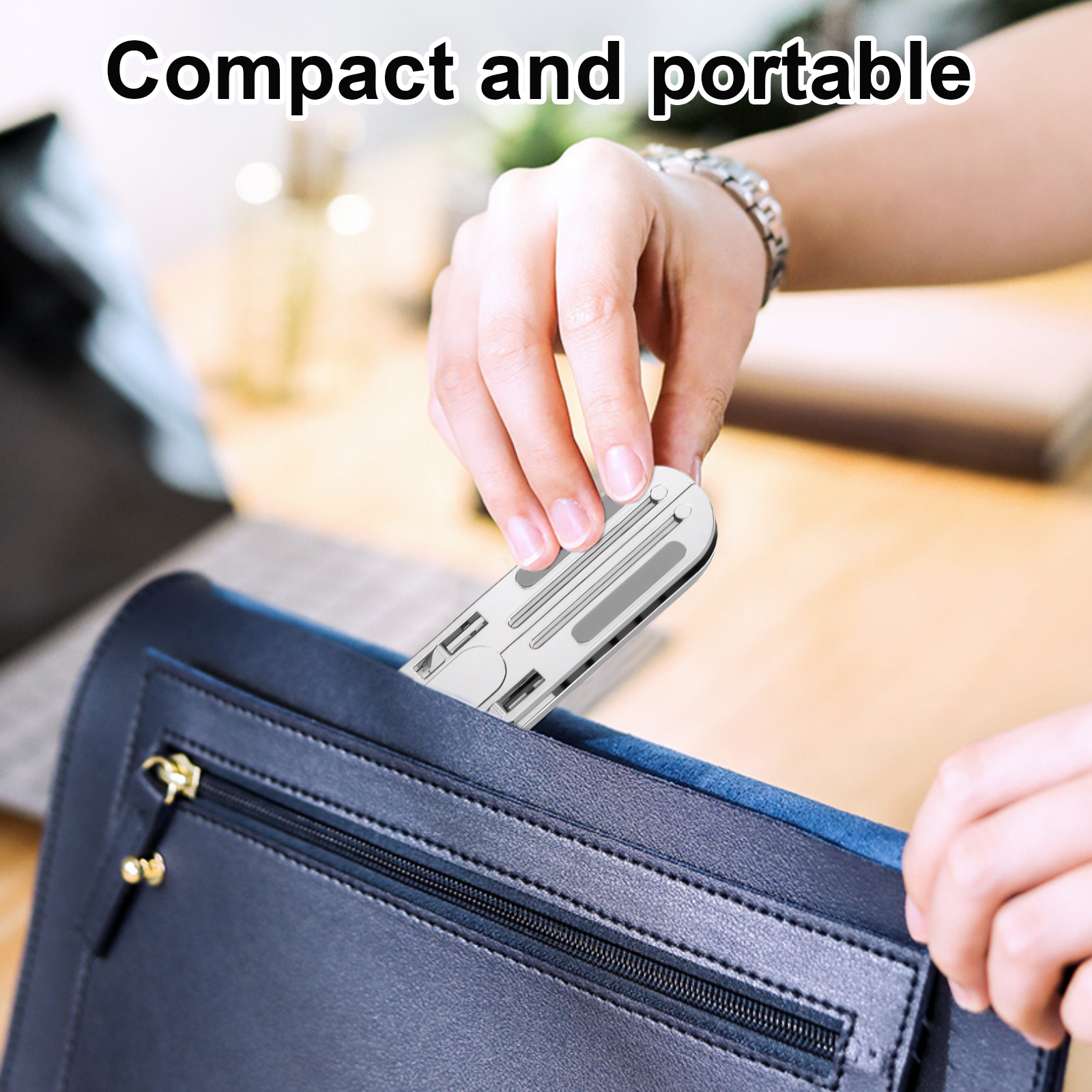 Eine Hand, die einen silbernen Laptopständer in eine schwarze Tasche auf einem Holztisch legt.
