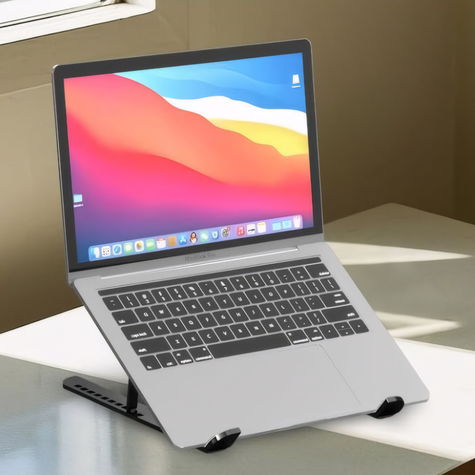 Laptop auf einem schwarzen Ständer. Der Laptop ist silberfarben und der Bildschirm ist eingeschaltet. Der Hintergrund ist weiß.