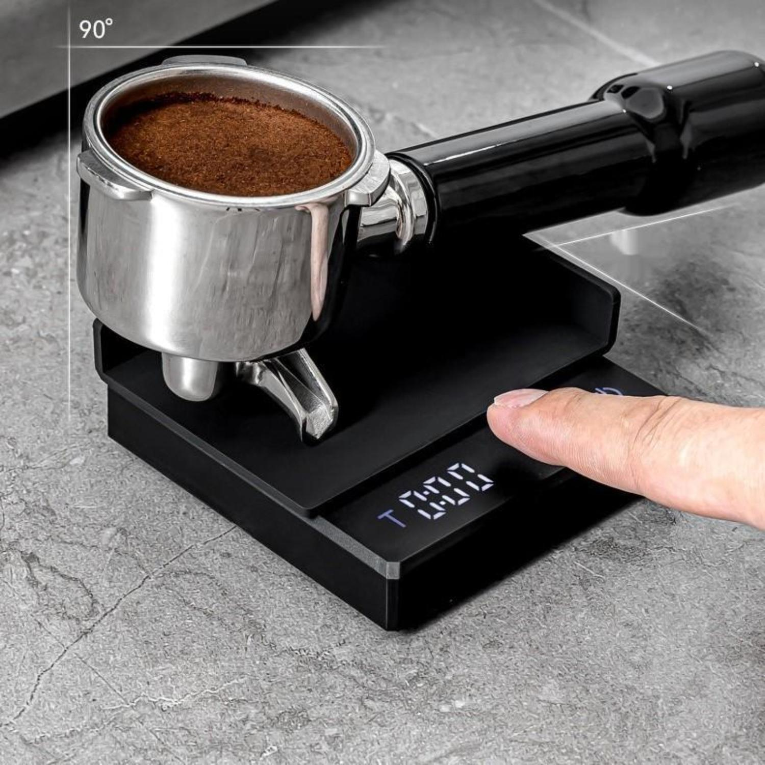 Nahaufnahme des Kaffeebrühens. Ein Siebträger mit Kaffeepulver liegt auf einer schwarzen Waage.