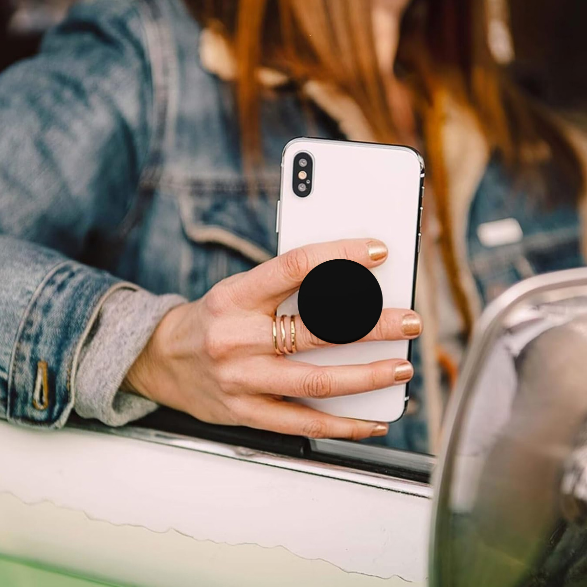Die Hand einer Frau mit goldenem Ring hält ein weißes Smartphone mit einem schwarzen runden Pop-Socket.