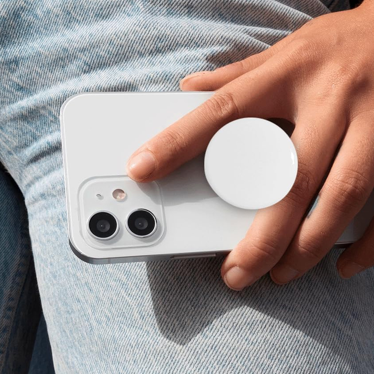 Eine Hand hält ein weißes Telefon mit einem weißen Pop-Socket auf der Rückseite. Die Person trägt Jeans.