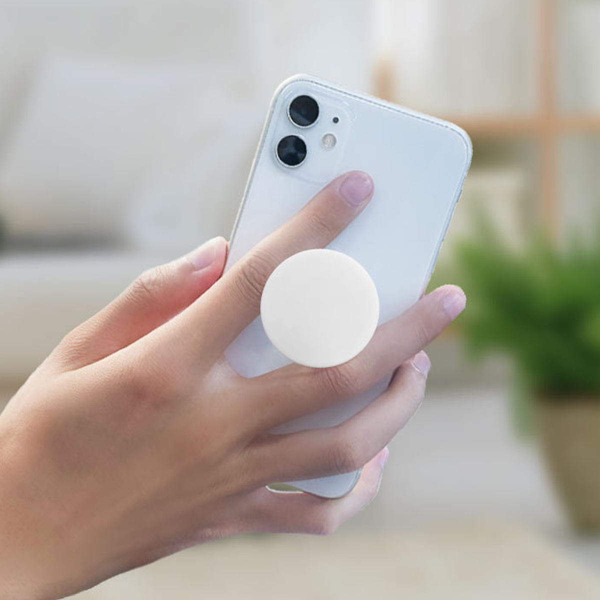 Ein weißes Telefon mit einem weißen Pop-Socket wird von einer Hand gehalten. Der Hintergrund ist unscharf.