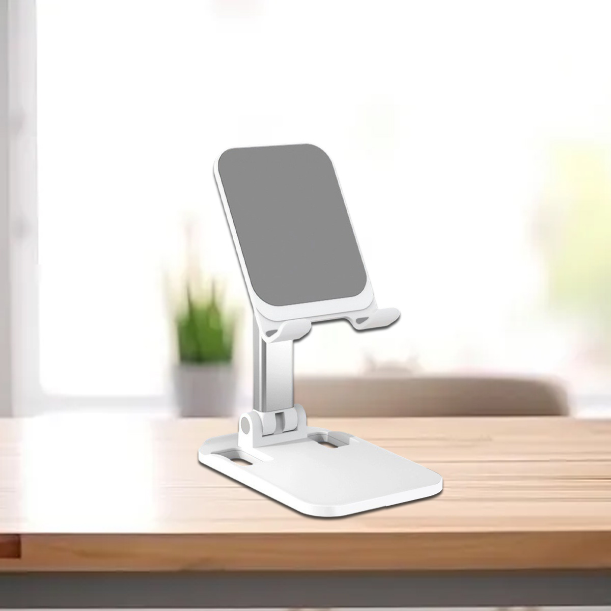 Ein weißer, zusammenklappbarer Telefonständer auf einem Holztisch mit verschwommenem Hintergrund und grüner Pflanze.