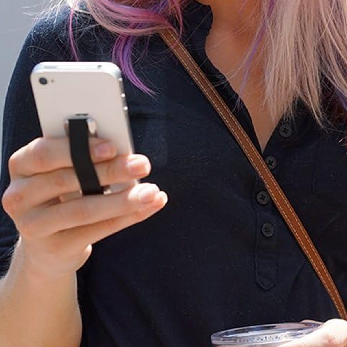 Die Hand einer Person, die ein weißes Telefon mit einem schwarzen Griffband hält. Die Person hat pinkes und lilafarbenes Haar.
