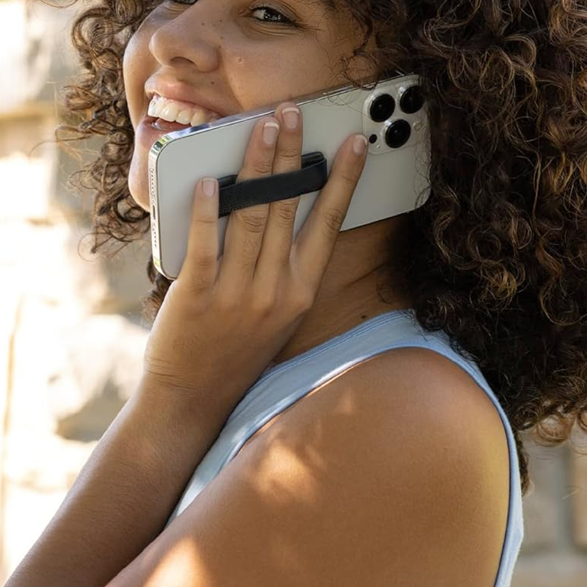 Eine Frau mit lockigem Haar hält ein Telefon mit einem schwarzen Handygriff. Sie lächelt.