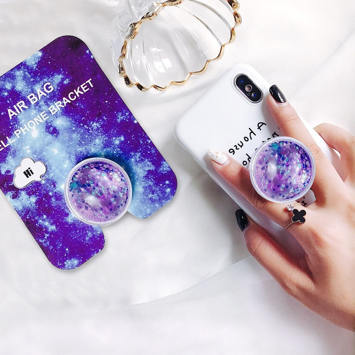Die Hand einer Frau, die ein Telefon mit einem Pop-Socket im Galaxien-Design hält.
