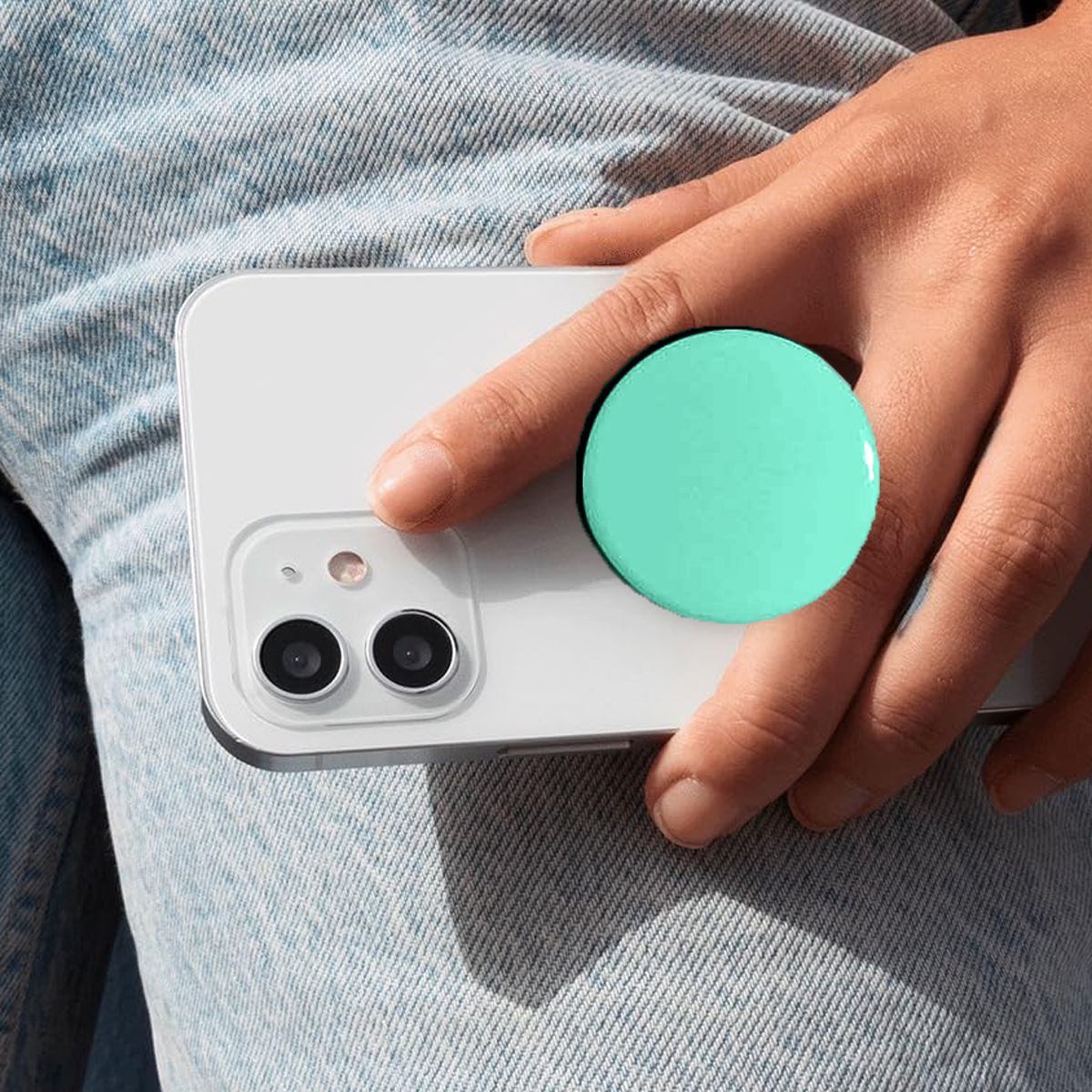 Eine Hand hält ein weißes Telefon mit einem grünen Pop-Socket. Das Telefon liegt auf Jeans.