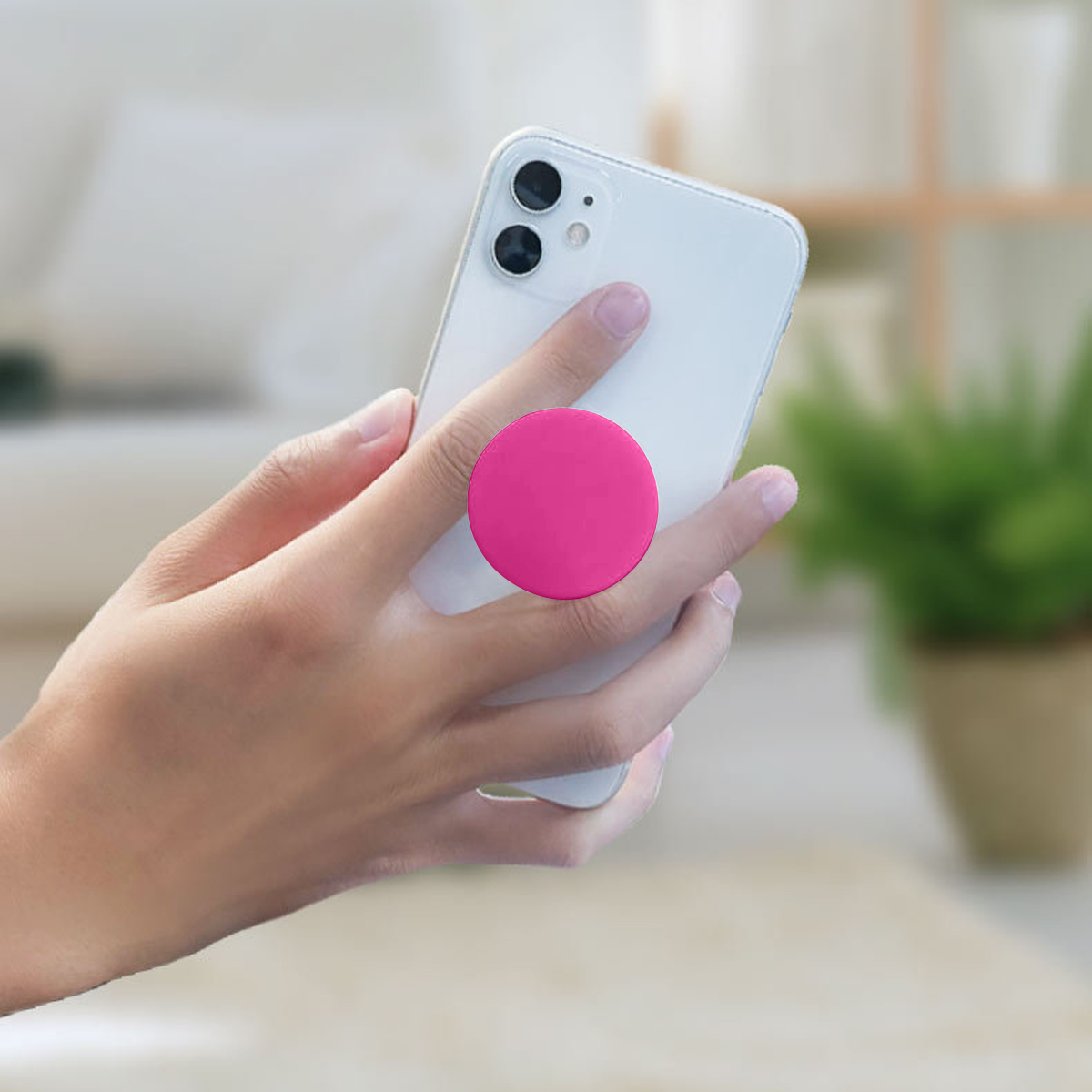 Hand hält ein weißes Smartphone mit einem pinken PopSocket, unscharfer Hintergrund.