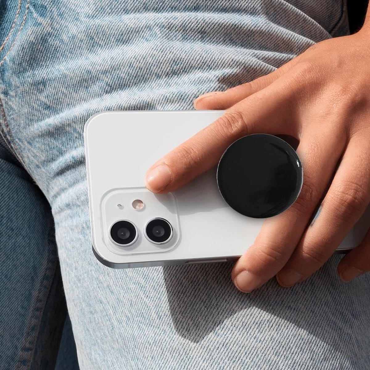 Eine Hand hält ein weißes Telefon mit einem schwarzen Pop-Socket. Der Pop-Socket ist auf der Rückseite des Telefons angebracht.